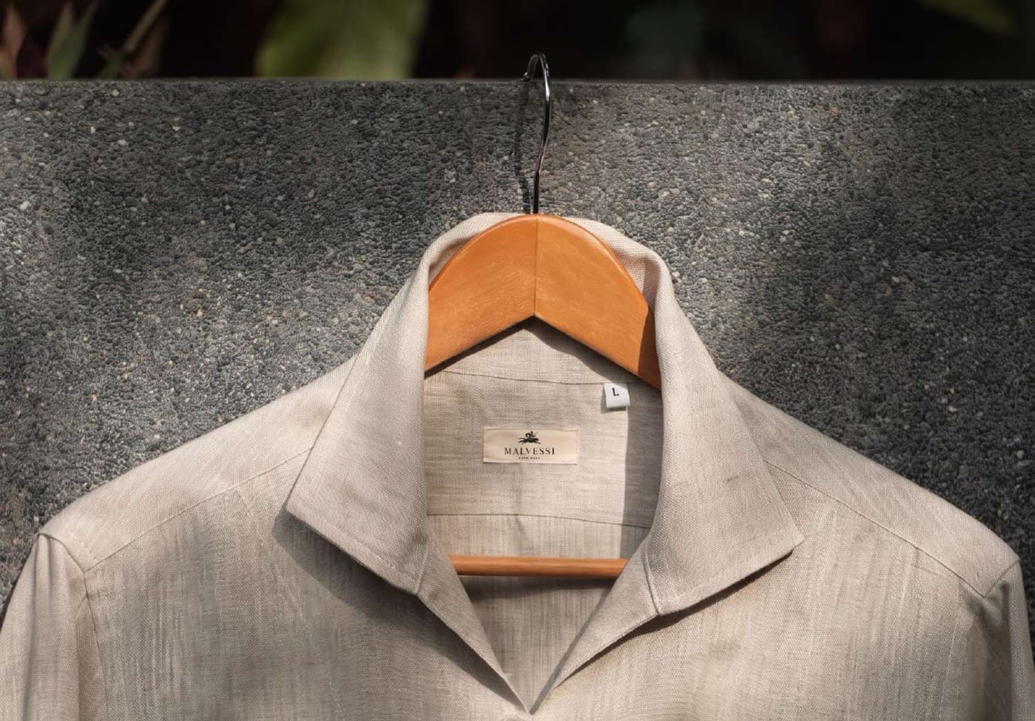 A Malvessi linen shirt on a wooden hanger against a stone wall